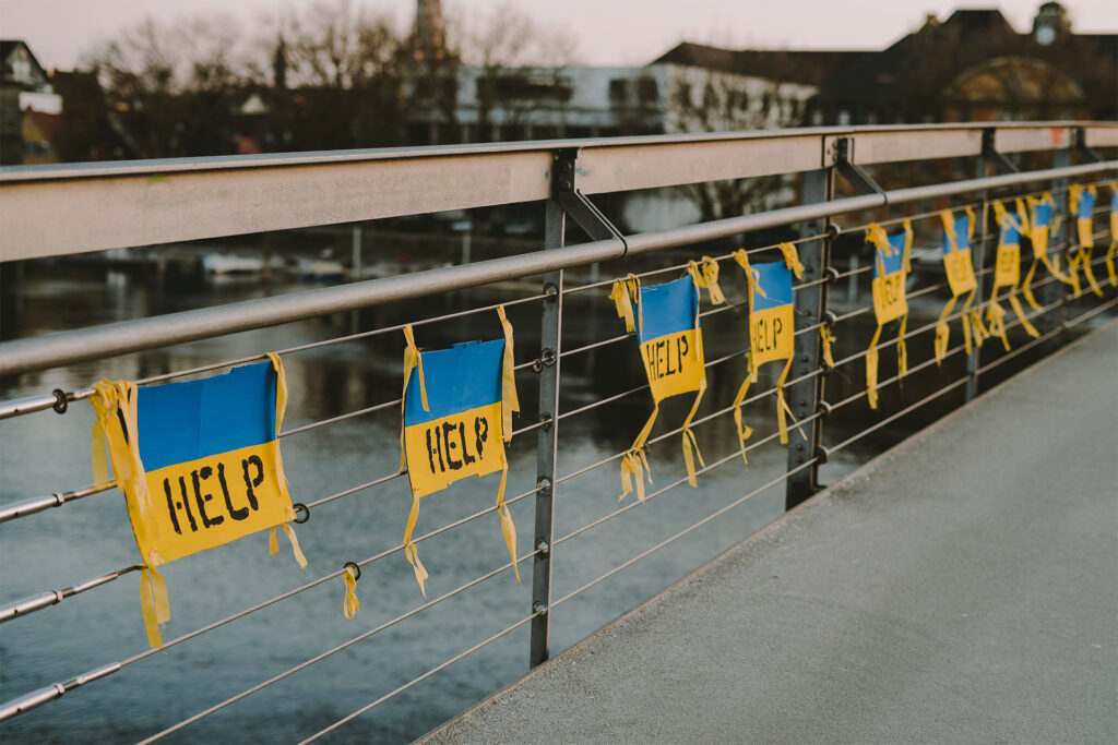 A row of Ukrainian flags with the word "help" hanging neatly on a bridge